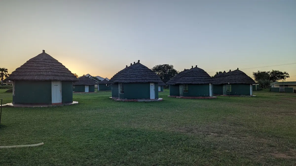 Round thatched guest huts on a lawn at dusk in Kidepo Valley